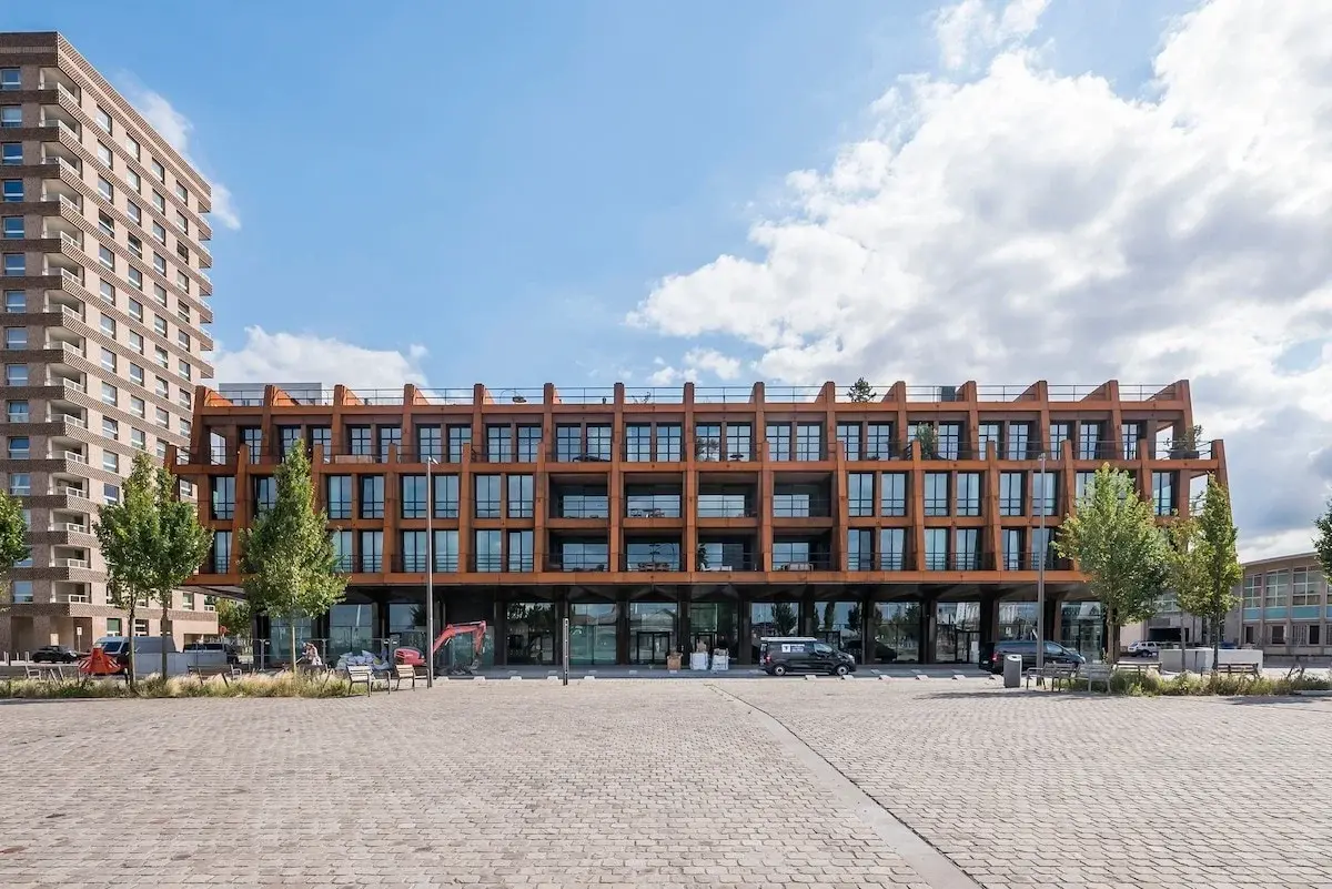 Modern appartementsgebouw met roestkleurige stalen gevel aan een bestrate plein