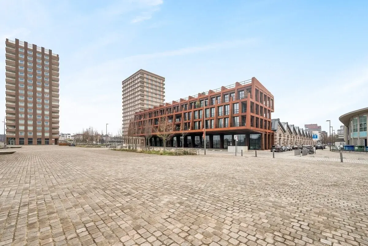 Modern appartementsgebouw met roestkleurige stalen gevel aan een bestrate plein