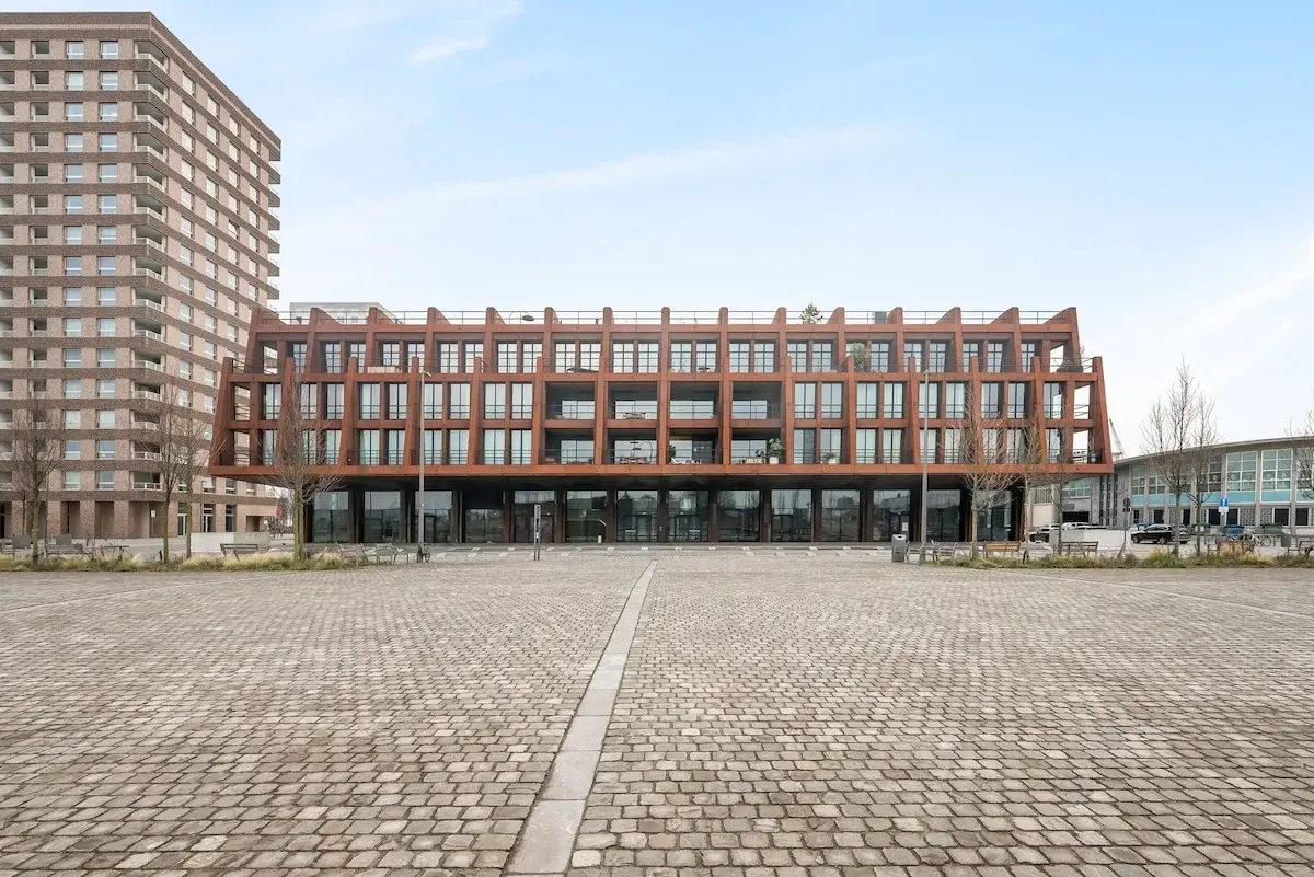 Immeuble moderne à façade en acier rouille donnant sur une place pavée